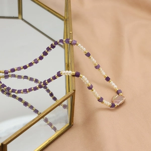 Baroque pearl necklace with purple amethyst stones and gold beads on a mirror box