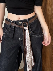 Detail of dark blue denim jeans with brown leather belt and paisley silk scarf accessory