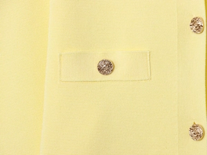 Close-up of knit cardigan showing yellow fabric texture and gold embossed metal buttons