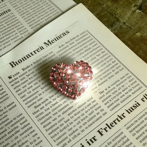 Pink heart-shaped brooch with sparkling crystals on vintage newspaper background