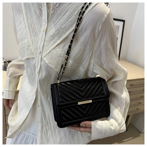 Classic black quilted shoulder bag with V-shaped stitching and gold chain strap worn by model