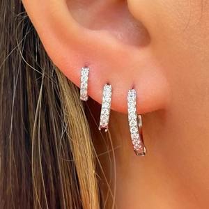Three-piece set of silver hoop earrings with pave-set crystals on model's ear