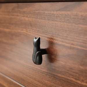 Minimalist black cast iron cat-shaped drawer handle on dark wood furniture surface