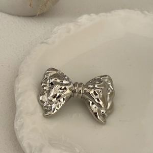 Close-up of a silver hammered metal bow hair accessory on a white ceramic plate