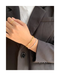 Close-up of gold vine woven bangle and stacked rings on model wearing black blazer