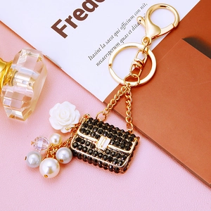 Detail of a gold keychain with black rhinestone purse charm and white resin flower