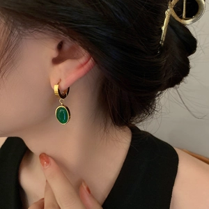Close-up of golden titanium emerald hoop earrings worn by a model in a natural light setting