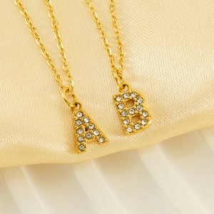 Colliers en acier doré avec pendentifs lettres en strass sur fond en soie élégante