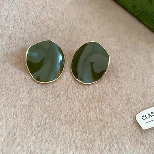 Detail view of 14k gold-plated irregular olive green enamel earrings on a textured background