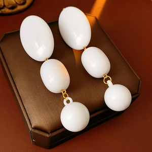 Detail of white geometric beaded earrings with gold links on brown leather jewelry box