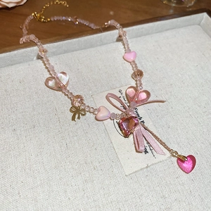 Detail of pink beaded necklace with resin hearts and metallic bow charm on fabric tray