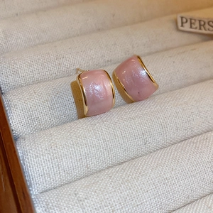 Detailed macro view of pastel pink pearlescent C-shaped stud earrings with gold plating