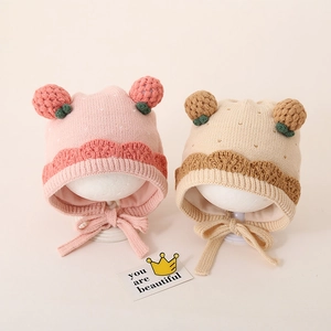 Gedetailleerd beeld van roze en beige gebreide baby mutsen met aardbeienpompons en veters