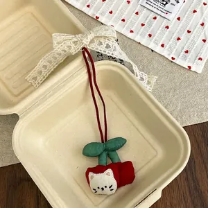 Detail of cute cherry cat plush charm with lace bow and embroidered details on red fabric