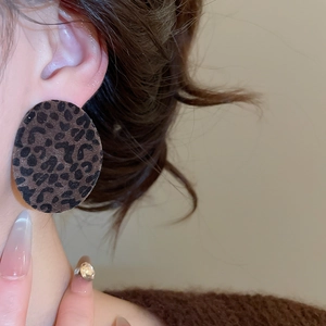 Close-up of a model wearing large oval leopard print flocked earrings with velvet texture