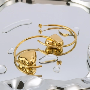 Polished 18K gold plated hollow heart-shaped hoop earrings on reflective surface