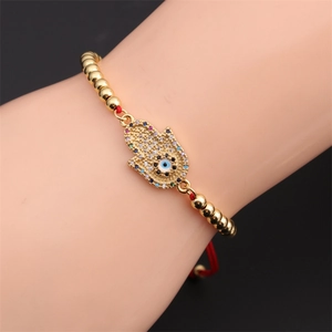 Macro view of gold Hamsa hand bracelet with zircon evil eye and red woven string