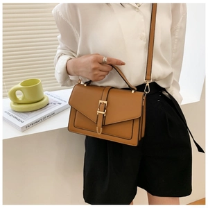Detailed view of a brown PU leather crossbody bag with gold hardware on a white desk