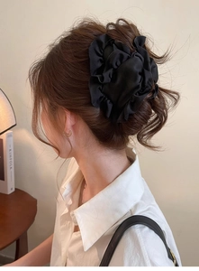 Black large pleated hair scrunchie shown styled on a model in a cozy indoor setting