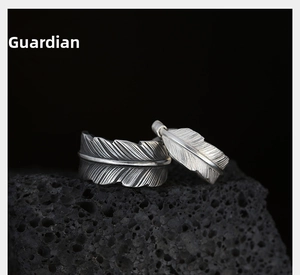 Detailed view of silver feather rings with intricate textures on black volcanic rock