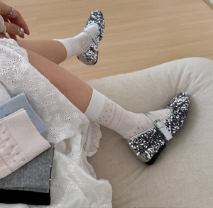 Close-up of floral hollow socks paired with silver sequin Mary Jane shoes on sofa