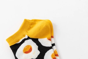 Detail of yellow cuff and heel on black ankle sock featuring fried egg patterns