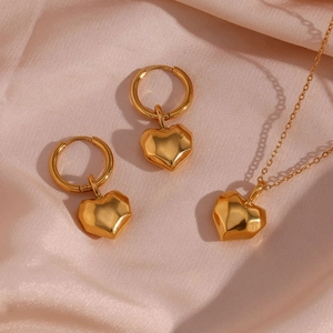 Close-up of golden 3D heart jewelry set on pink silk showing necklace and earrings