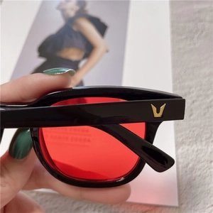 Close-up of black frame sunglasses with red lenses and golden V-shaped logo detail