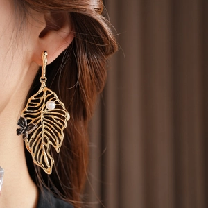 Close-up of golden hollow leaf earring with white pearl and butterfly on model