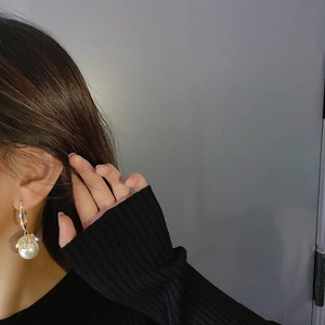 Detail of gold pearl earring with zircon ring accent on model with black outfit