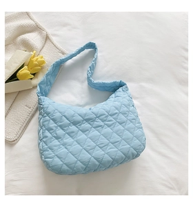 Detailed view of light blue quilted nylon shoulder bag on white textured backdrop