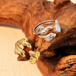 Minimalist 18k gold and silver open rings in leaf design displayed on a natural wooden branch