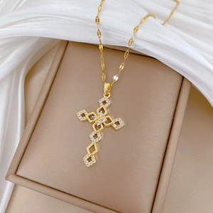 Detailed view of gold cross pendant with cubic zirconia on a beige jewelry box
