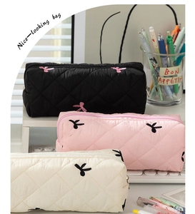 Detailed view of quilted bow pencil cases in black, pink, and beige with embroidery