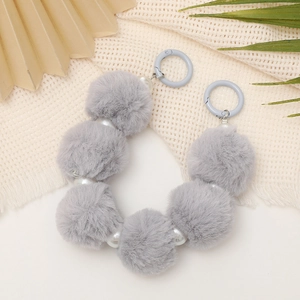 Detail view of gray pompom and pearl bead chain strap with metal clasps on fabric