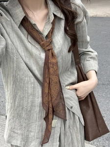 Gros plan du collier foulard en soie marron avec motifs paisley et texture de tissu