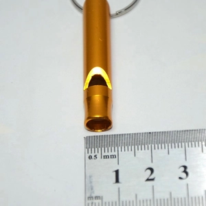 Orange aluminum survival whistle with key ring next to a steel ruler for size reference