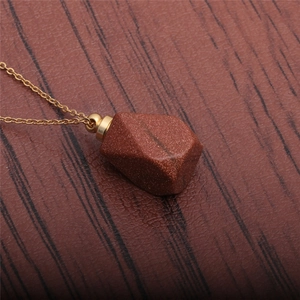 Goldstone perfume bottle pendant necklace with faceted design on wooden background