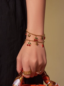 Détail de bracelets à pendentifs cerise et cœur dorés au poignet avec bagues fleur