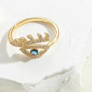 Close-up of golden geometric ring with blue evil eye zircon on white stone