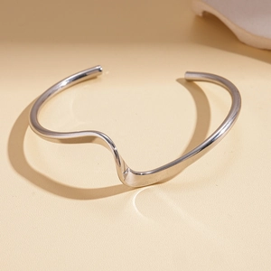 Macro view of polished silver wavy bangle showing irregular geometric curves and high gloss