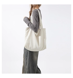 Detail view of a creamy white corduroy tote bag showing textured fabric on a model's shoulder