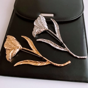 Detailed view of tulip brooches in gold and silver with textured metal petals on black leather