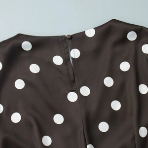 Vue détaillée de l'encolure ronde et du bouton au dos d'une robe à pois noirs