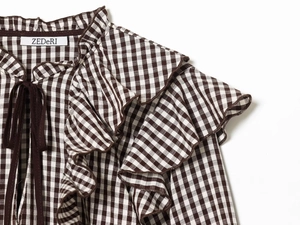 Close-up of ruffled high neck and tie detail on brown plaid long sleeve cotton shirt