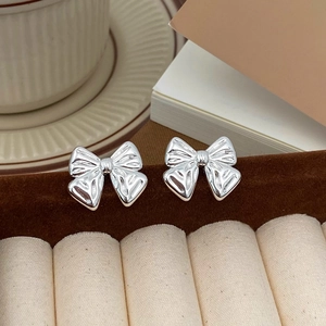 Detailed close-up of shiny silver bow earrings on a brown velvet jewelry display stand