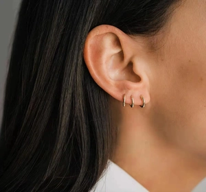 Close-up of three small golden hoop earrings worn by a model in a minimalist style