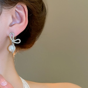 Close-up of model wearing silver bow pearl earrings with shimmering cubic zirconia stones