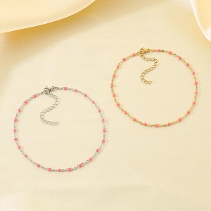 Close-up of gold and silver anklets with pink resin beads on soft beige silk fabric