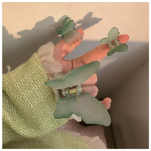 Detail of matte bean green butterfly hair clips set held in hand for size comparison